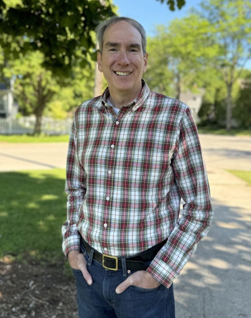 Jamie Wall standing outside with a flannel shirt under the shade of a tree